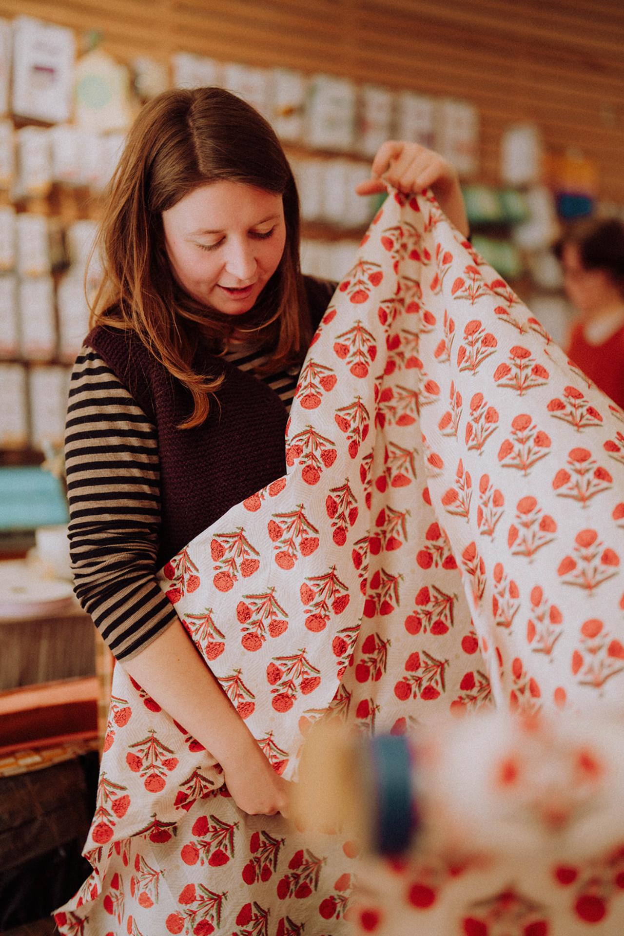 Meg is unrolling a cotton fabric with red floral pattern ready to cut