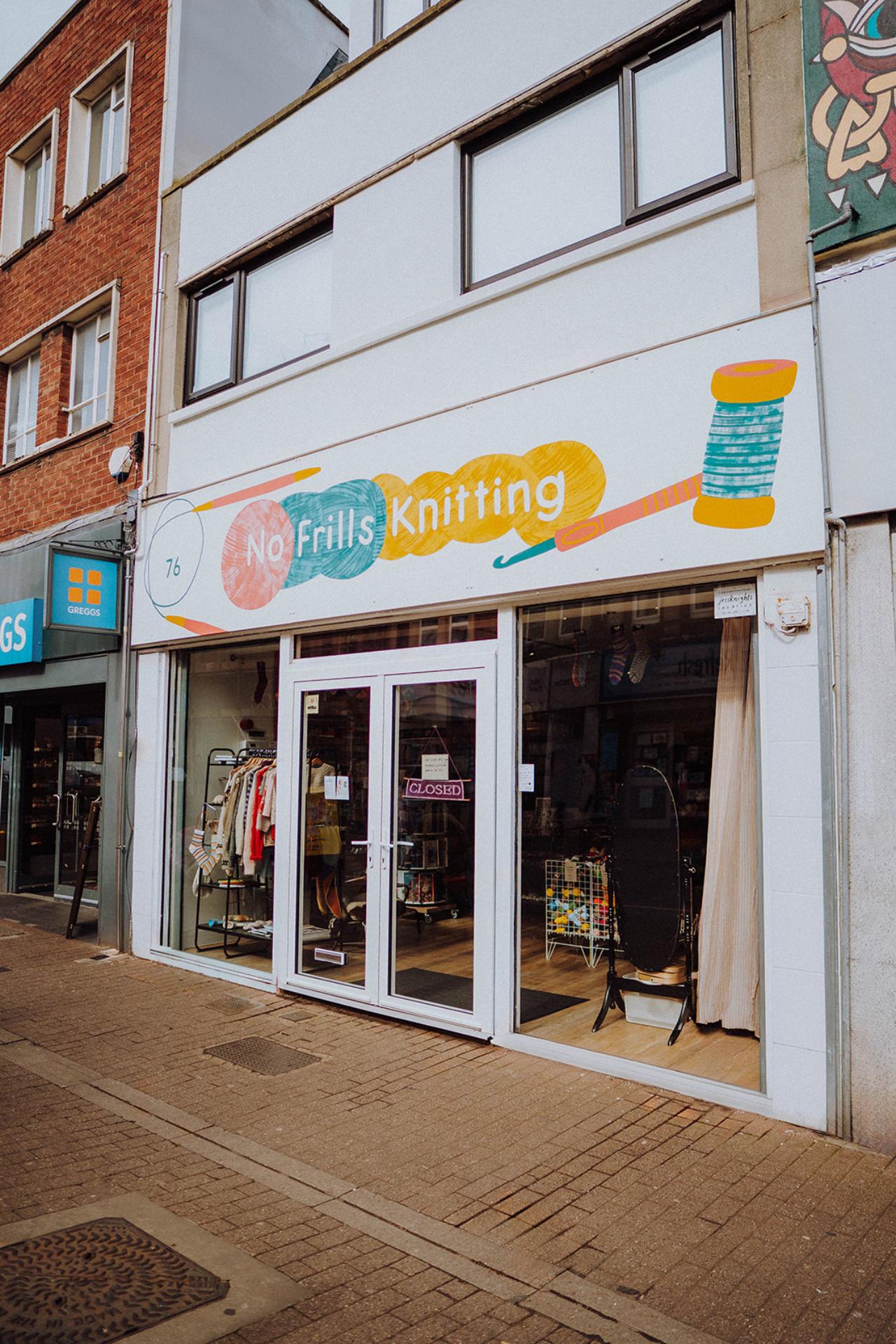 the front of no frills knitting on East Street in Bedminster. The shop sign is clearly visible and greggs is just in view to the left.